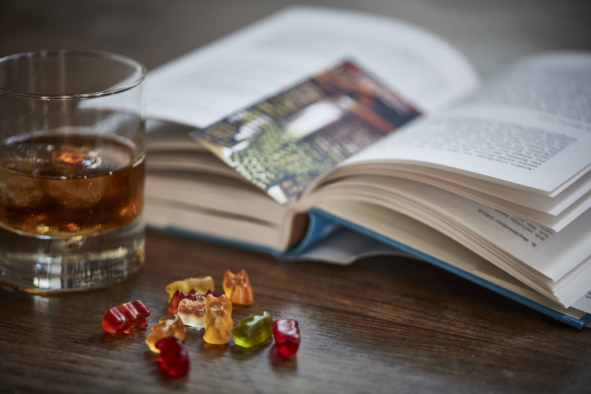 Verre d'alcool avec glaçon sur table avec livre et bonbons oursons en gomme