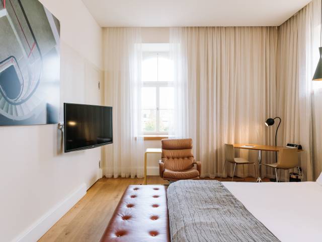 Chambre avec TV au mur, fauteuil et table de coin du B2 Hôtel de Zurich