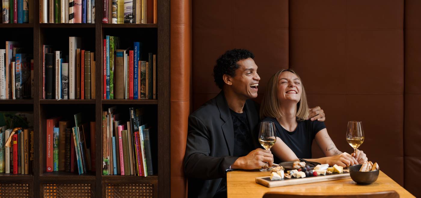 Couple sitting comfortably in a niche of the library and enjoying a wine & cheese pairing