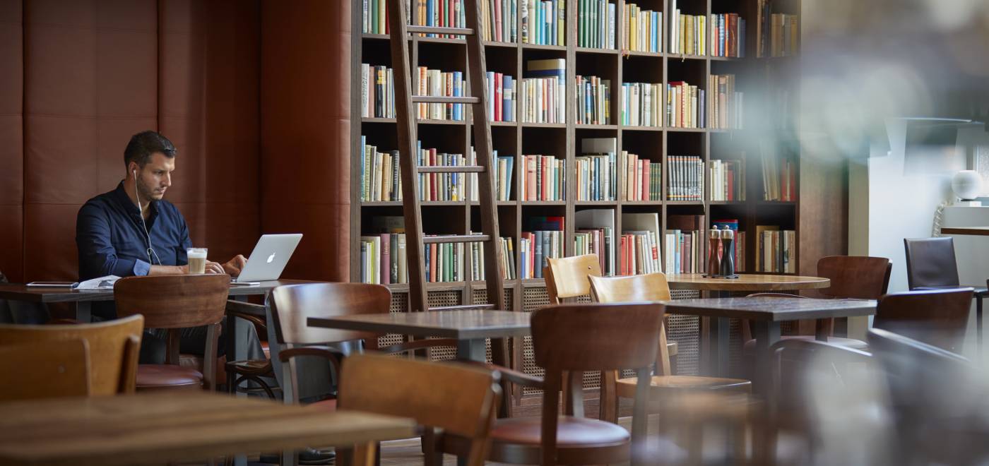 Homme assis avec un ordinateur portable et un café dans la bibliothèque du B2 Hôtel de Zurich