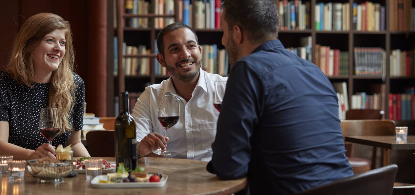 Personen sitzen an einem Tisch und genießen Wein und Käse