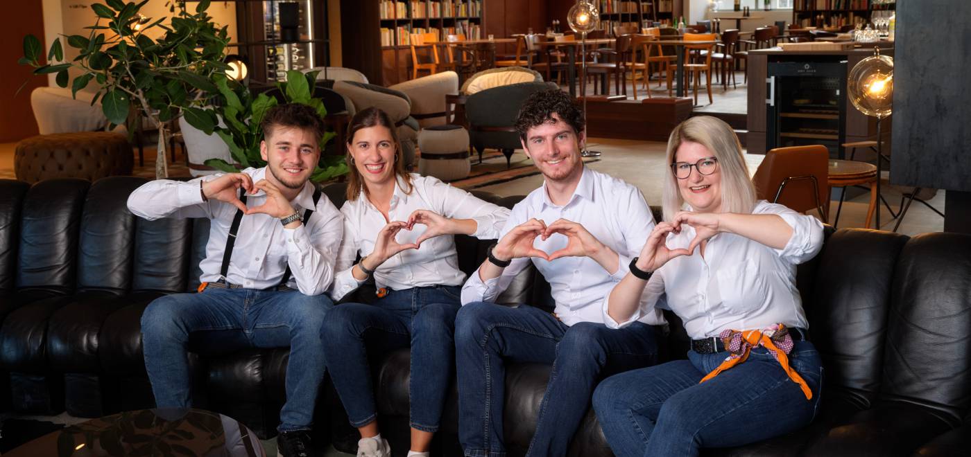 Guest Ambassadors auf Sofa formen mit Händen ein Herz