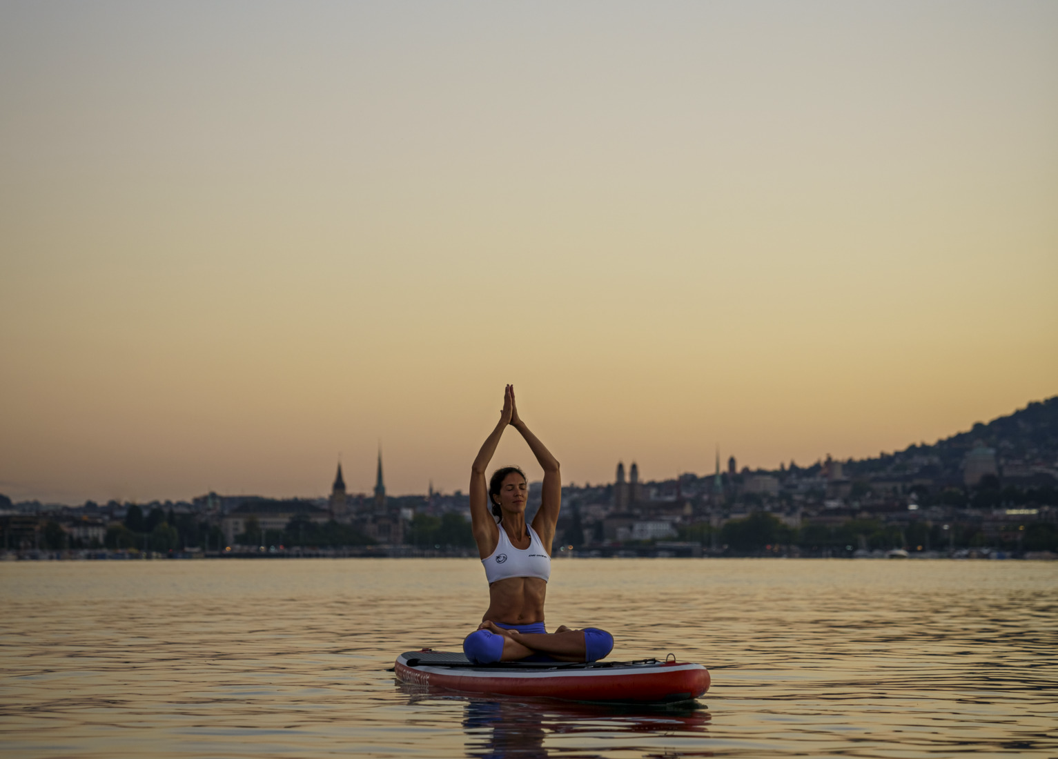 Frau im Yogasitz auf SUP auf dem Zürichsee bei Dämmerung