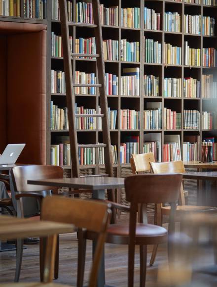 Homme assis avec un ordinateur portable et un café dans la bibliothèque du B2 Hôtel de Zurich