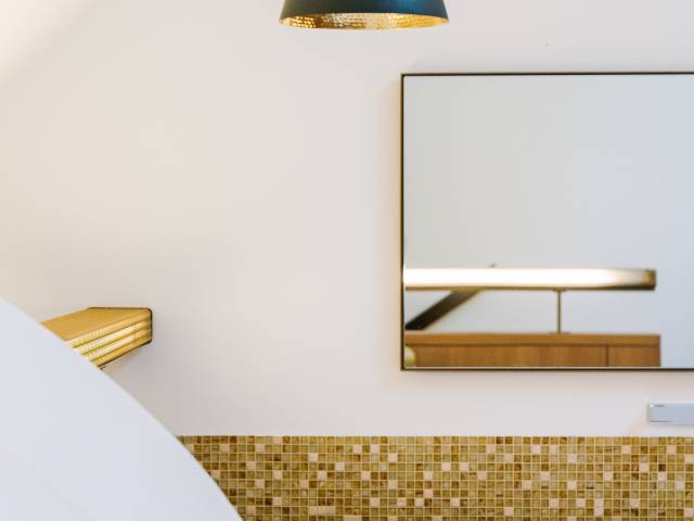 Großer quadratischer Spiegel an der Wand und moderne Lampe über der Badewanne in einem Zimmer des B2 Hotels Zürich.